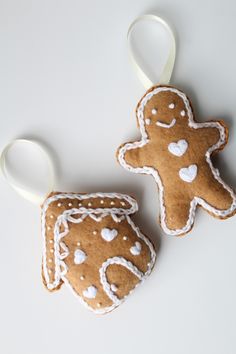 two gingerbread cookies with white icing and hearts are on a white table top