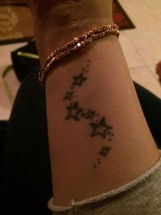 a woman's arm with stars on it and a gold bracelet around her wrist