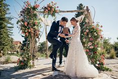 a bride and groom are getting married in front of an arch with flowers on it