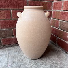 a white vase sitting in front of a brick wall