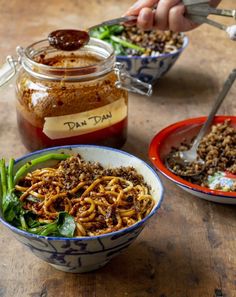 two bowls filled with food sitting on top of a wooden table next to jars and spoons