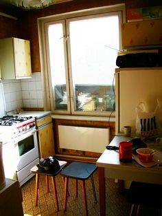 a small kitchen with an oven, stove and table in the corner by the window