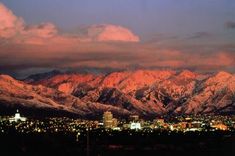 the city lights are on in front of snow covered mountains and buildings at night time