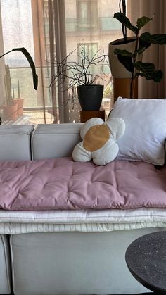 a couch with pillows and a stuffed animal sitting on it's back in front of a window