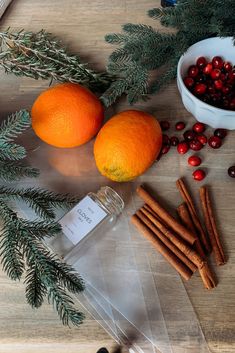 oranges, cinnamon sticks, and spices on a wooden table next to a bowl of cranberries