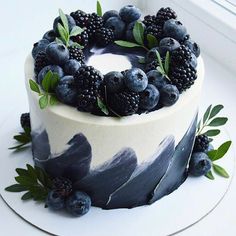 a white cake with blackberries and blueberries on top is sitting in front of a window