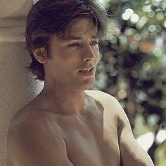 a shirtless man leaning against a wall with his hand on his hip and looking off to the side