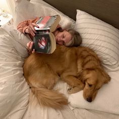 a woman laying in bed next to a dog with a book on it's head