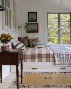 a bed sitting under a window next to a wooden table with flowers on top of it