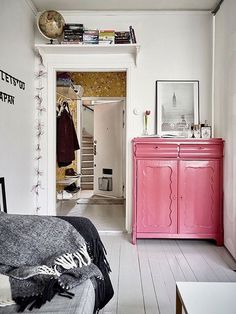 a bedroom with white walls and pink furniture in the foreground, an open door leading to another room