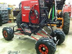 a red and black machine on wheels in a room with other equipment behind it,