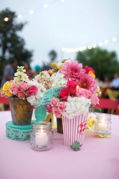 flowers in vases on a table with candles and tea lights for the centerpiece