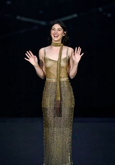 a woman in a gold dress with her hands out to the side on a dark background