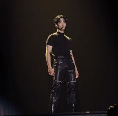 a man standing on top of a stage wearing black leather pants and boots with his mouth open