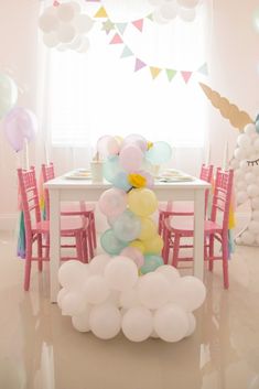 the table is set with balloons and chairs for an unicorn themed birthday party in pastel colors