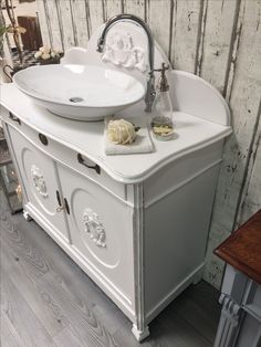 a white sink sitting on top of a wooden floor next to a wall mounted faucet