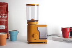 a yellow blender sitting on top of a counter next to cups and coffee bags