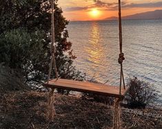 a wooden bench sitting on top of a grass covered hillside next to the ocean at sunset