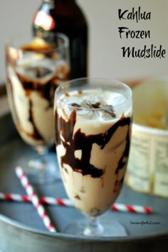 two glasses filled with ice cream on top of a metal tray next to a bottle