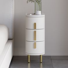 a white cabinet with two drawers and a vase on it next to a bed in a room