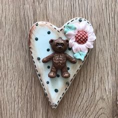 a heart shaped object with a teddy bear and flower on it's side sitting on a wooden surface