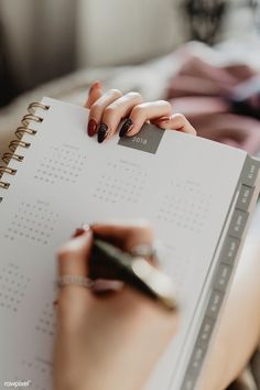 a woman's hands holding a calendar and pen on top of a book that is open