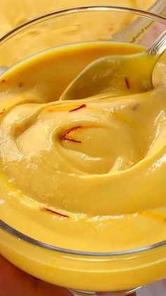 a person holding a spoon in a glass bowl filled with yellow liquid and orange peels