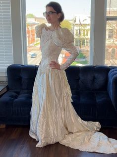 a woman standing in front of a blue couch wearing a white dress with long sleeves