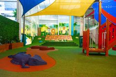 An indoor sheltered childcare that floor's covered in mostly grass except the red rubber the animal props are on. The sandpit has grass covered steps leading up to it and the rectangular climbing wall is at the back. Early Childhood Playground, Inclusive Indoor Playground, Primary School Playground, Aussie Childcare Network, Climbing Walls, Business Hub, Kids Cafe