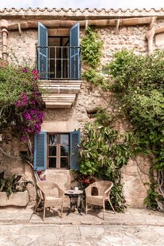 an old building with blue shutters and flowers on the outside, along with tables and chairs