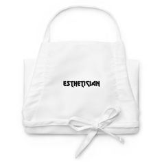 an embroidered white apron with the word esthetian printed on it and tied in a bow