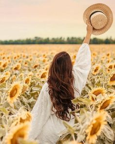 a woman standing in a field of sunflowers with her arms up to the sky