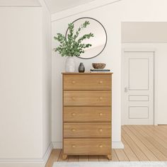 a white room with a dresser, mirror and potted plant on the top shelf