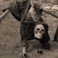 an old man with a skull on his back in the grass next to a dead animal