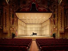 an empty auditorium with red seats and a piano on the stage in front of it