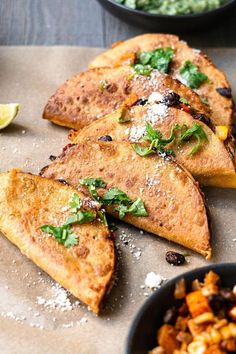 three quesadillas on a cutting board next to bowls of salsa and lime wedges