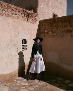 a woman standing in front of a adobe building