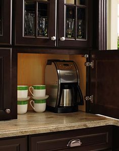 a coffee maker and two cups are on the counter in this small kitchen with dark wood cabinets