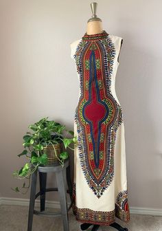 1970s sleeveless bohemian maxi dress. Dashiki style print, floor length and high neck collar. Back plastic zipper with hook and eye closure above zipper. Print is red, blue, green, yellow, orange. Fabric is off white. Beautifully tailored with bust darting and tapering at waist. Dress has some lining.  Tag: None  SIZE  Modern size: S Bust: 36" Waist: 29" Hip: 38" Length: 55" Measurements are taken with the garment lying flat, and un-stretched. Bust, waist and hip measurements are doubled. Sleeve Printed Floor-length Maxi Dress For Festivals, Retro Multicolor Printed Maxi Dress, White Sleeveless Boho Print Maxi Dress, Bohemian Fitted Floor-length Maxi Dress, Hippie Floor-length Maxi Dress, Fitted Boho Print Maxi Dress In Hippie Style, Fitted Sleeveless Hippie Dress, Bohemian Maxi Dress With Vintage Print, Multicolor Floor-length Maxi Dress For Festival