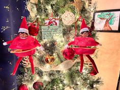 two elfs are sitting on top of a christmas tree in front of a sign