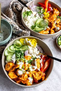 two bowls filled with different types of food on top of a white table cloth next to a bowl of rice and cucumbers