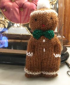 a knitted teddy bear with a green bow tie and hat sitting in front of a mirror