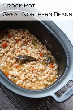 a crock pot filled with beans and carrots next to a spoon in it