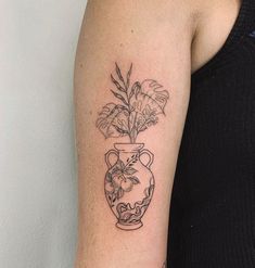 a woman with a tattoo on her arm has a vase with flowers and leaves in it