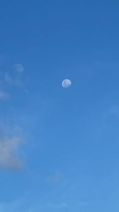 an airplane flying in the blue sky with a half moon behind it and some clouds