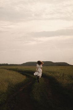 a woman in a white dress is running down a dirt road with her hair blowing in the wind