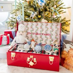 a christmas tree is in the background with presents under it and an open red suitcase