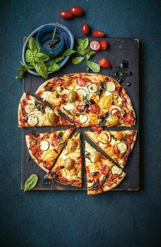 a pizza cut into eight slices on top of a cutting board with tomatoes, zucchini and basil