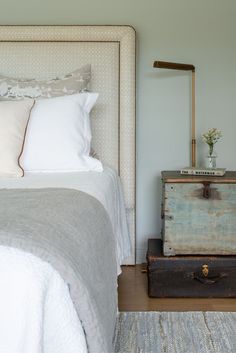 an old trunk sitting on the floor next to a bed with white sheets and pillows