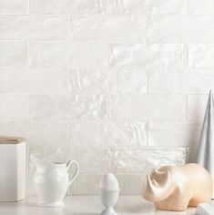 three white vases sitting on top of a counter next to a box and other items